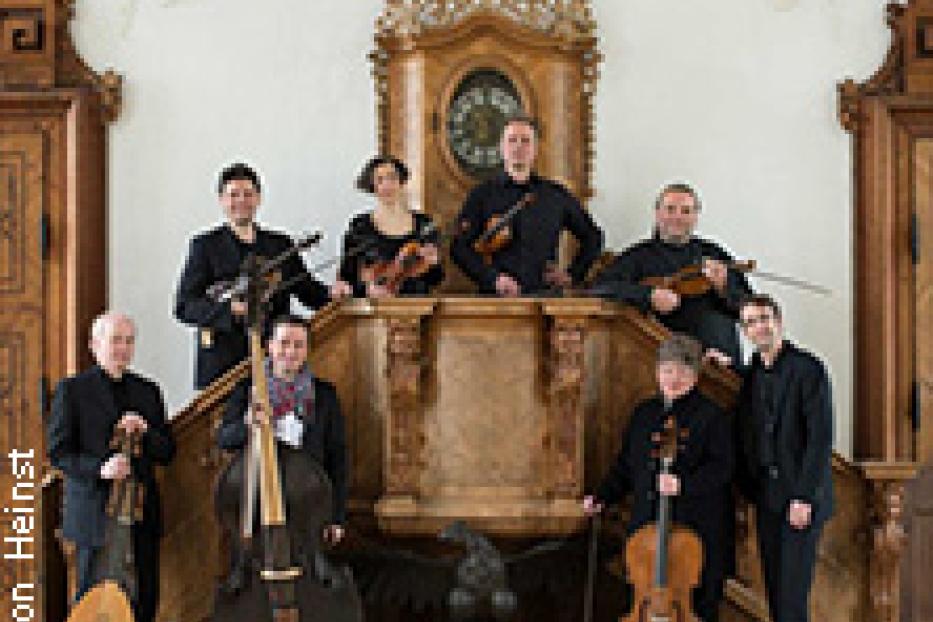 Ein Ensemble mit historischen Instrumenten posiert auf einer Treppe vor einer verzierten Uhr.