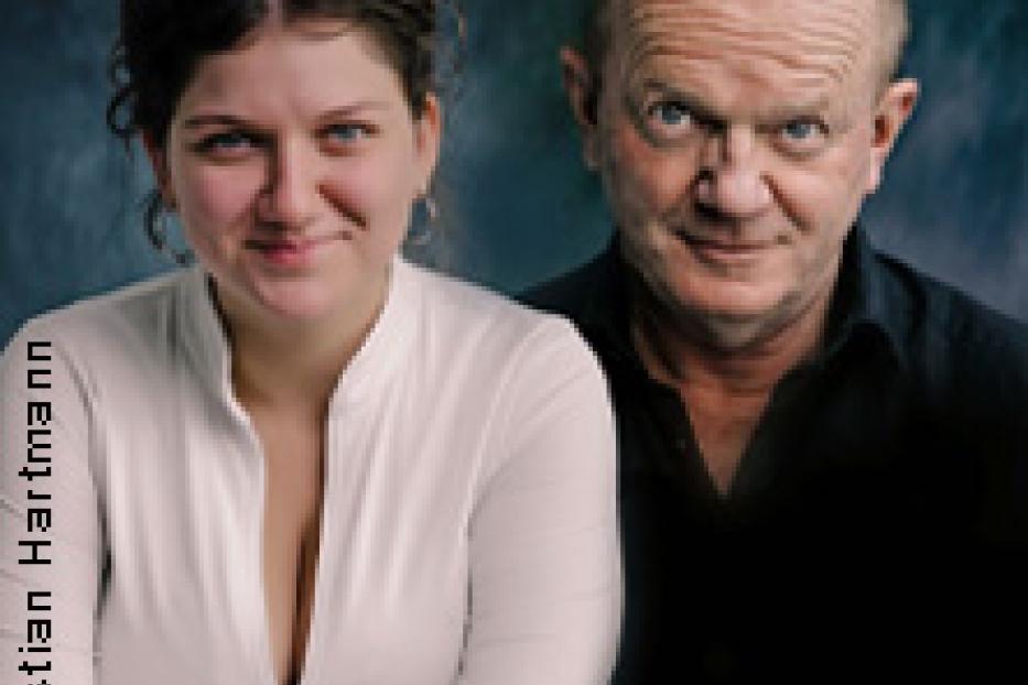 Ein Porträt einer jungen Frau und eines älteren Mannes vor einem dunklen Hintergrund.