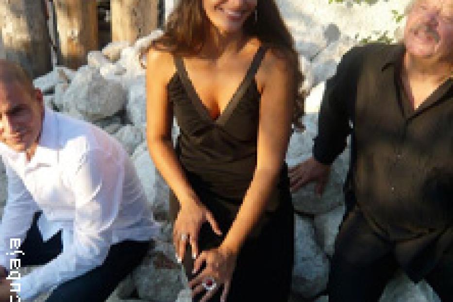 Eine Frau in einem schwarzen Kleid posiert mit zwei Männern vor einem Steinhaufen.