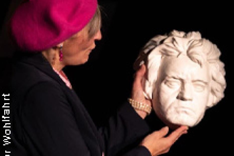 Eine Frau mit roter Baskenmütze hält eine Büste von Ludwig van Beethoven.