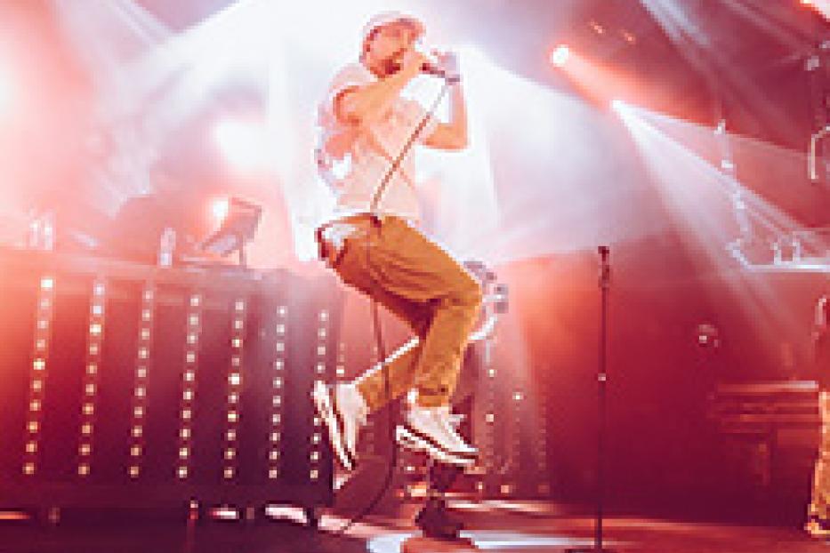 Ein Sänger springt mit einem Mikrofon in der Hand auf einer Bühne.