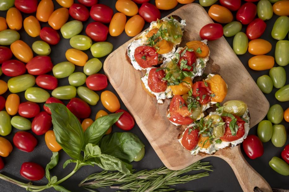 Ein Holzschneidebrett mit einer Ansammlung von Tomaten und frischen Kräutern.
