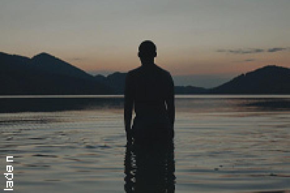 Eine Person steht im Wasser vor einer Bergkulisse im Abendlicht.