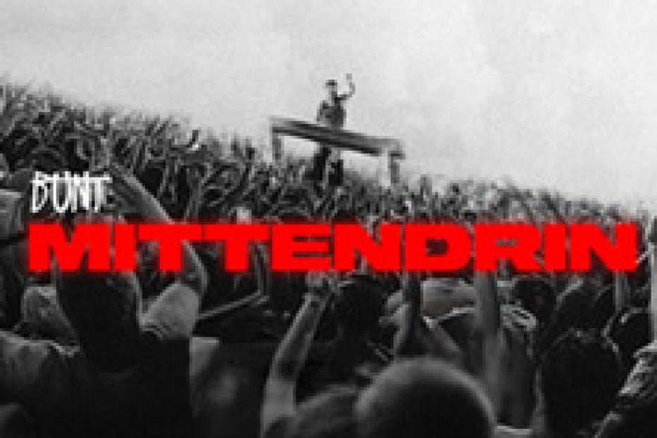 Eine Menschenmenge jubelt vor einer Bühne inmitten eines Feldes.