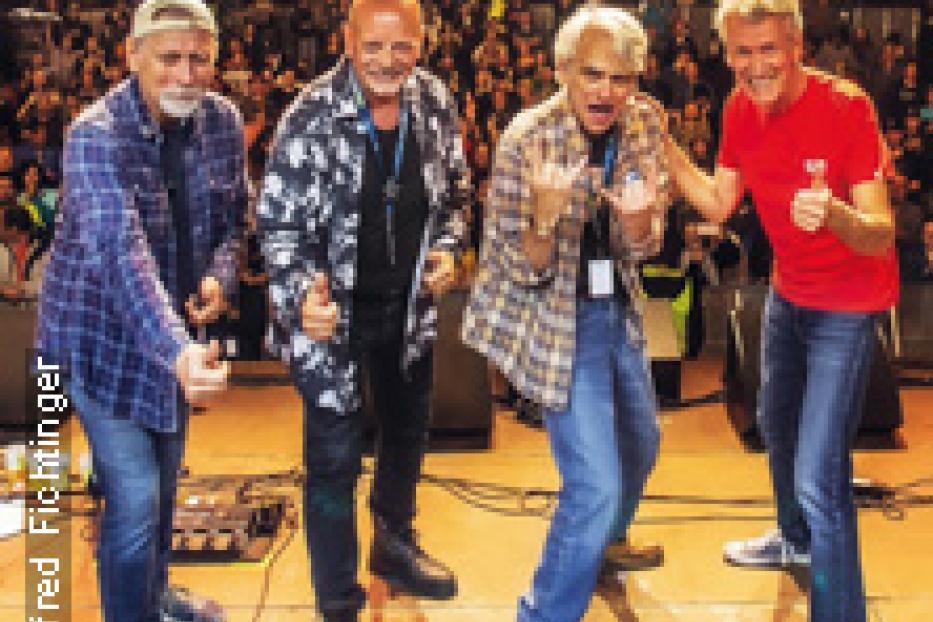 Eine Band posiert auf einer Bühne vor Publikum.