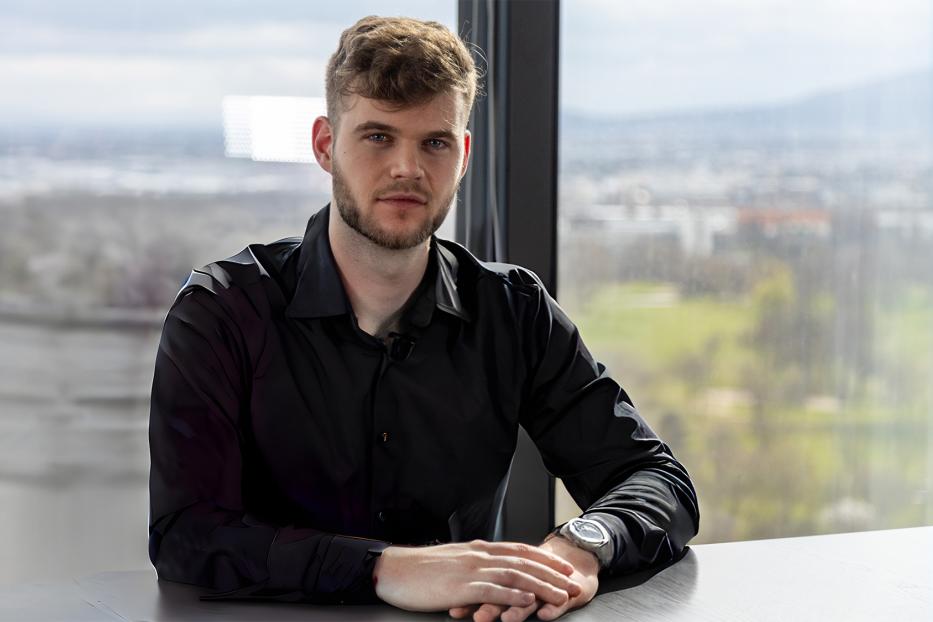 Ein Mann in einem schwarzen Hemd, der an einem Konferenztisch vor einem Fenster sitzt. 