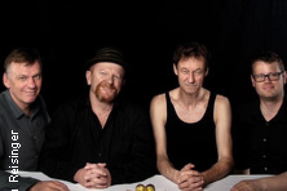 Vier Männer sitzen an einem Tisch mit einer goldenen Dekoration in der Mitte.