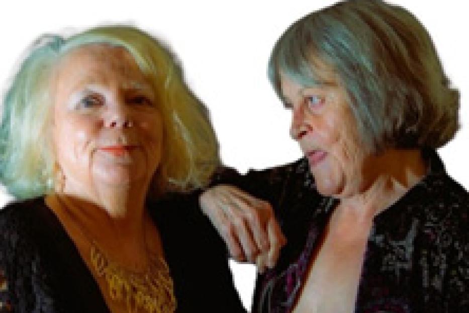 Zwei ältere Frauen stehen nebeneinander und lächeln.