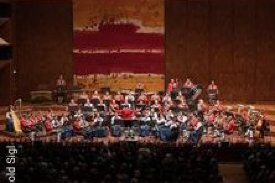 Ein großes Orchester spielt auf einer Bühne vor einem Publikum.
