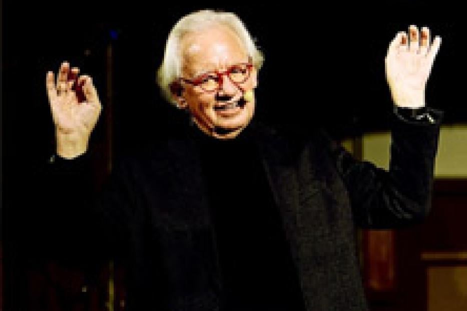 Ein älterer Mann mit Brille gestikuliert mit erhobenen Händen.