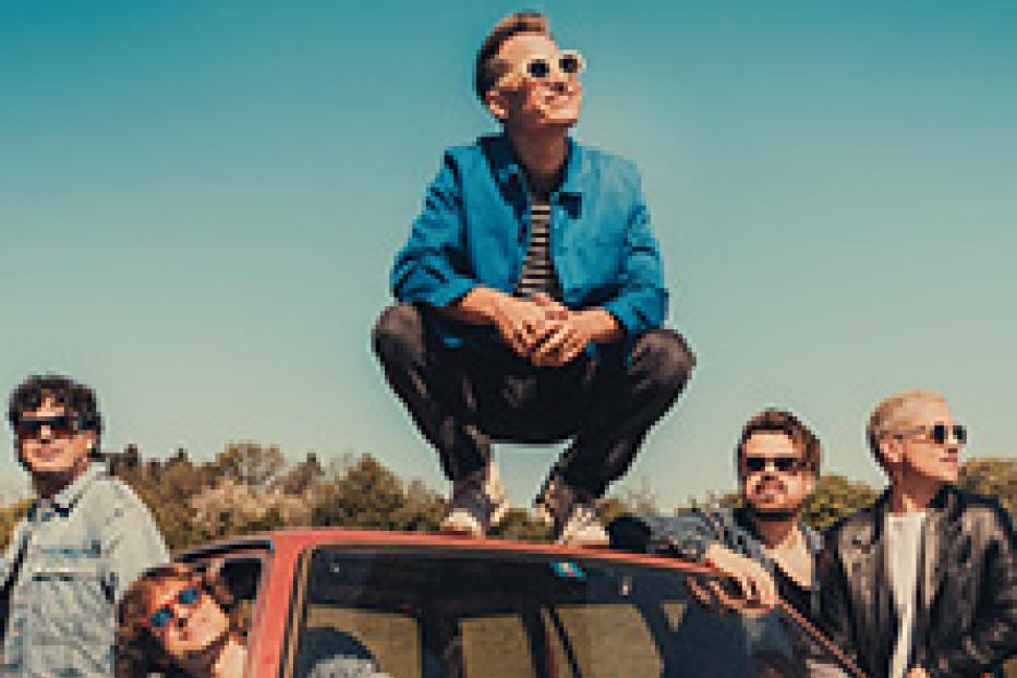 Die Band Giant Rooks posiert auf und an einem roten Auto vor blauem Himmel.