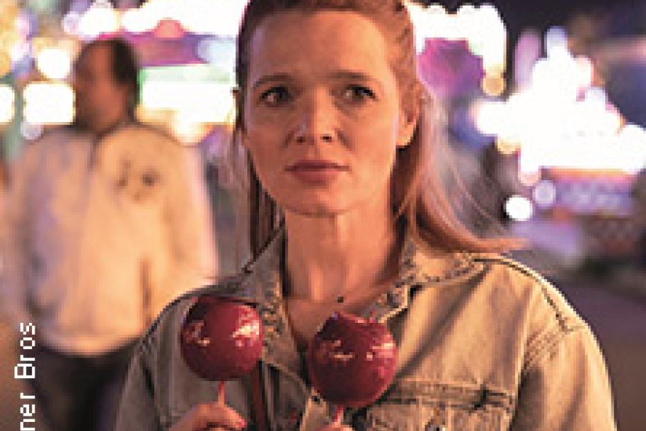 Eine Frau hält zwei rote Zuckeräpfel auf einem Jahrmarkt.