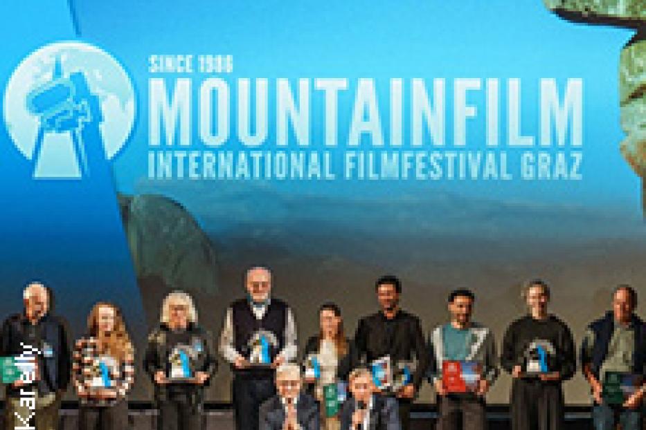 Eine Gruppe von Menschen steht auf einer Bühne vor dem Mountainfilm International Filmfestival Graz Logo.