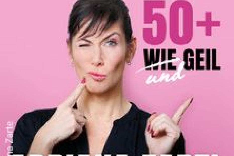 Adriana Zartl posiert vor einem pinkfarbenen Hintergrund mit dem Schriftzug „50+ WIE GEIL und“.