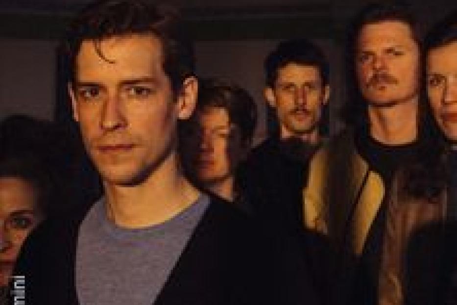 Eine Gruppe junger Erwachsener steht zusammen, der Mann im Vordergrund blickt in die Kamera.