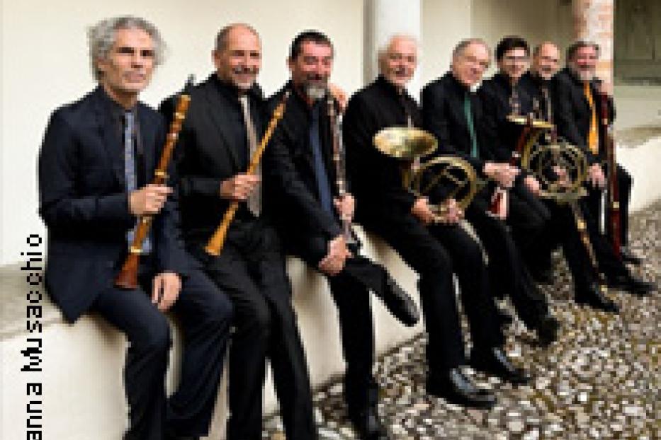 Eine Gruppe von acht Musikern sitzt mit ihren Instrumenten auf einer Mauer.