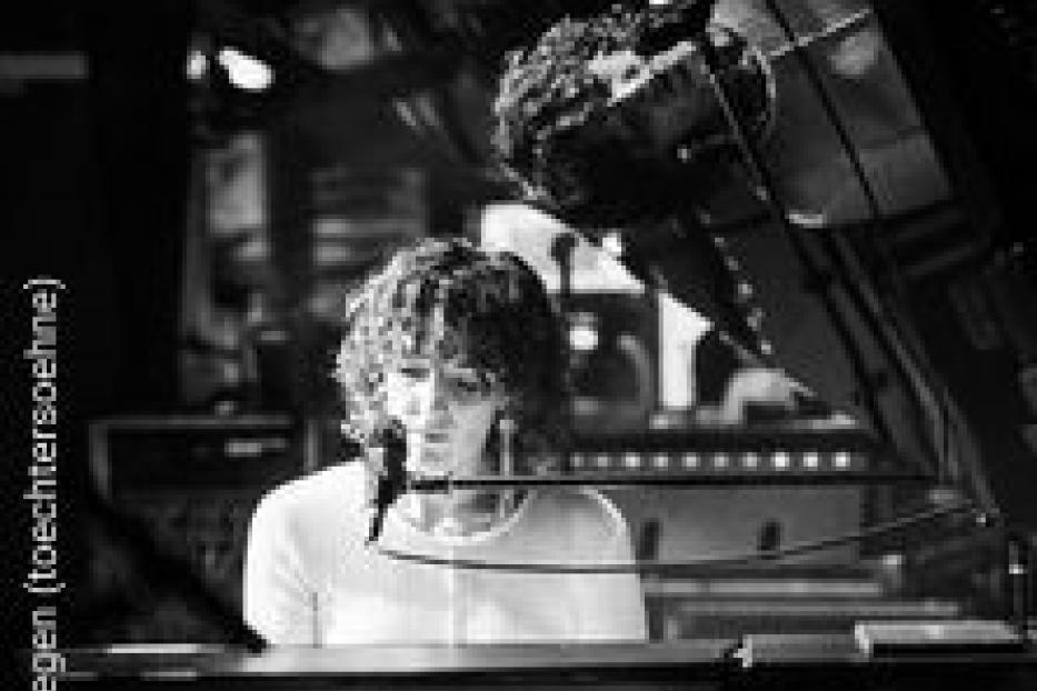 Eine Frau mit lockigem Haar spielt Klavier vor einem Mischpult.