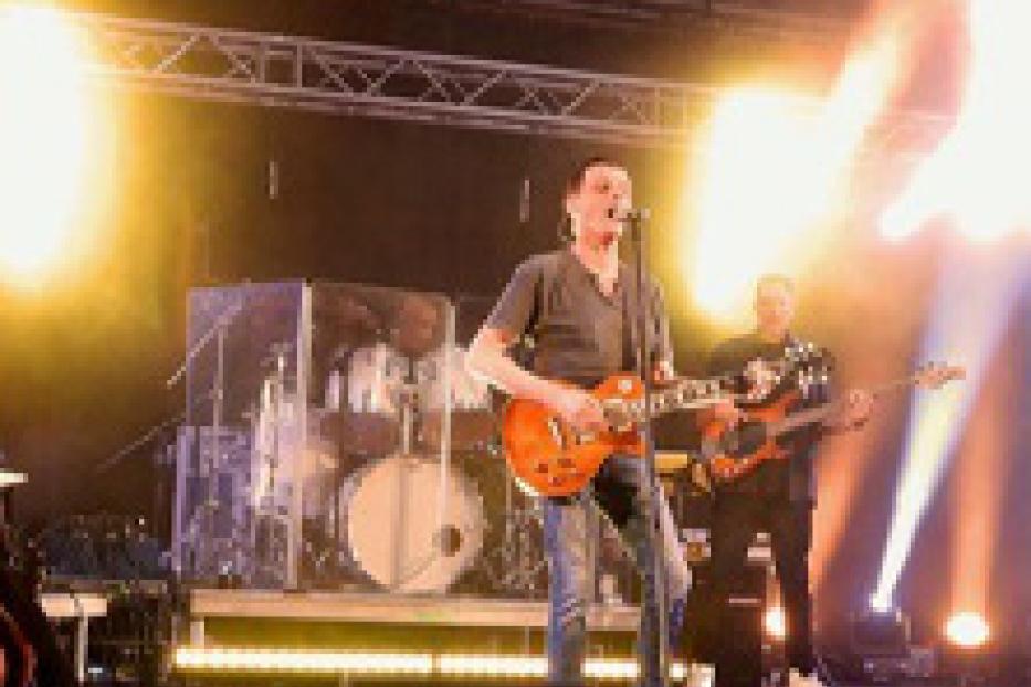 Ein Gitarrist steht auf einer Bühne während eines Konzerts.