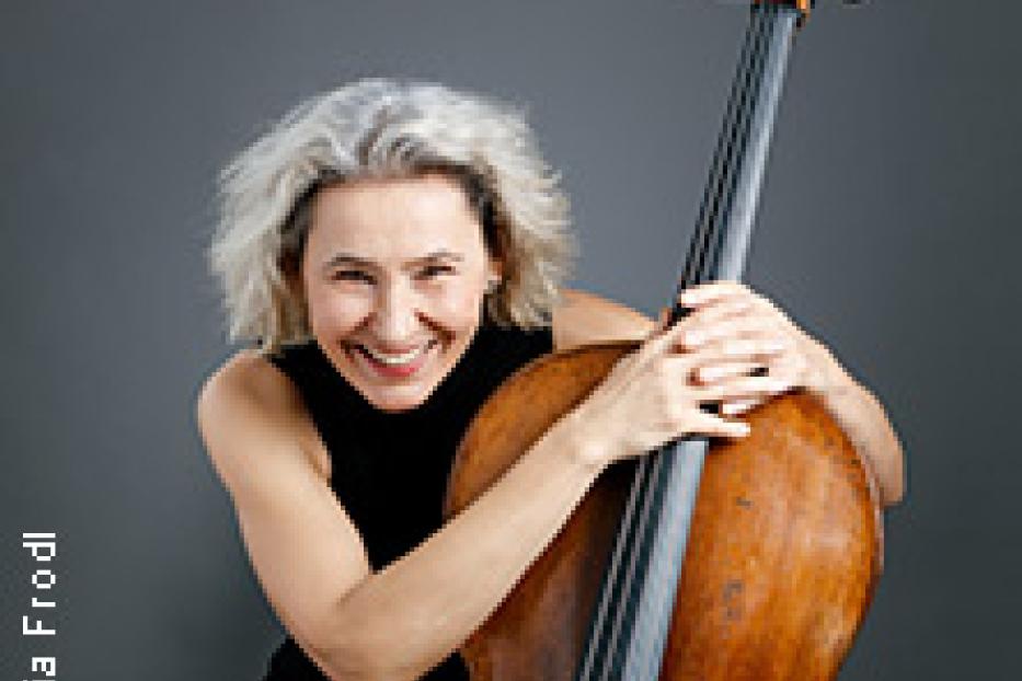 Eine lächelnde Frau mit grauem Haar umarmt ein Cello.
