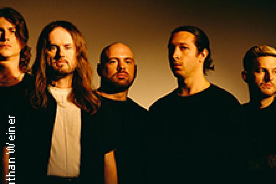 Fünf Männer stehen vor einem dunklen Hintergrund.