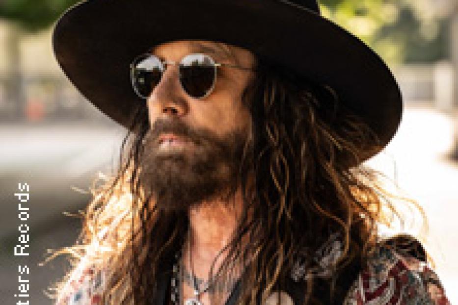 Ein Mann mit Bart, Hut und Sonnenbrille posiert für ein Foto.