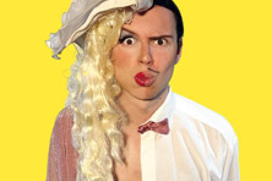 Ein Mann mit Make-up und einer Perücke, zur Hälfte in Damen- und zur Hälfte in Herrenkleidung gekleidet.