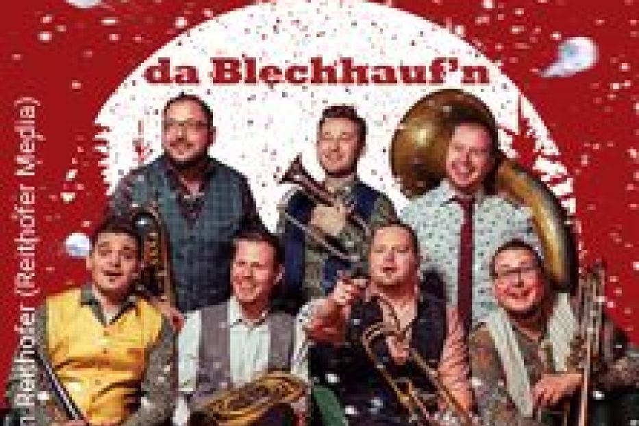 Die Blaskapelle „da Blechhauf’n“ posiert vor einem weihnachtlichen Hintergrund.
