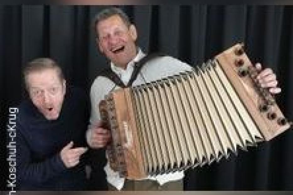 Zwei Männer posieren mit einer Steirischen Harmonika vor einem schwarzen Vorhang.
