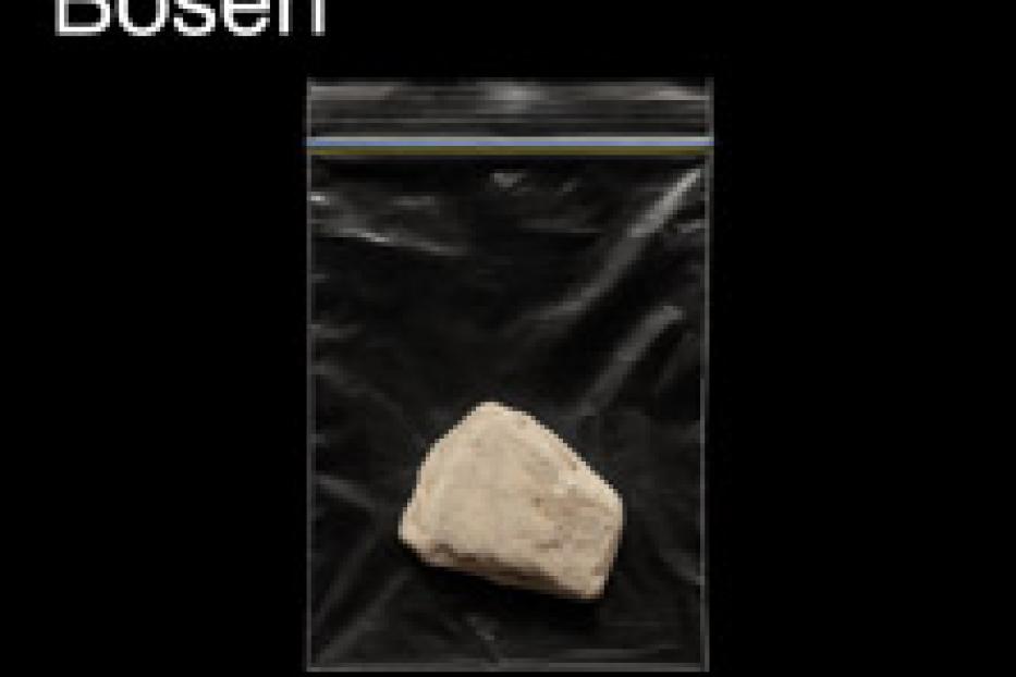 Ein Stein in einer Plastiktüte vor schwarzem Hintergrund, Teil der Ausstellung „Die Farben des Bösen“.