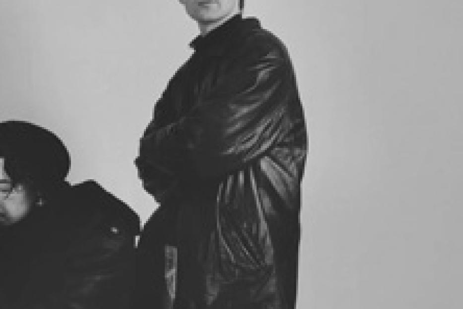 Ein Mann mit verschränkten Armen in einer schwarzen Jacke vor einem hellen Hintergrund.