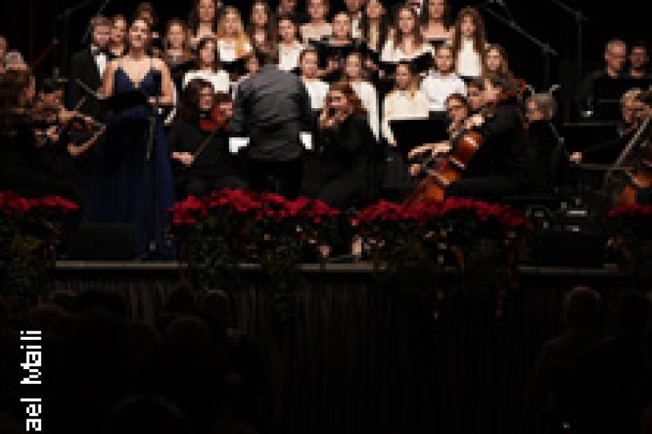 Ein Chor und ein Orchester treten auf einer Bühne vor einem Publikum auf.