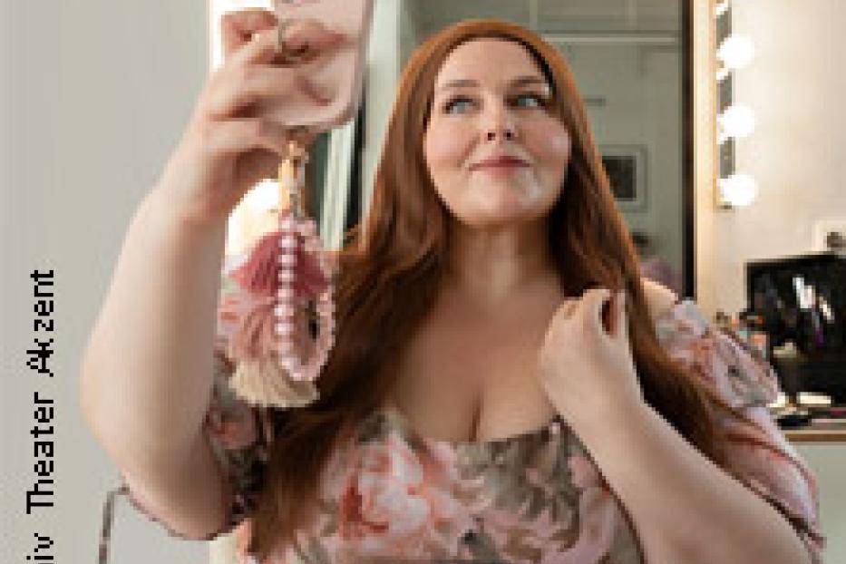 Eine Frau mit langen, roten Haaren macht ein Selfie in einem blumigen Kleid.