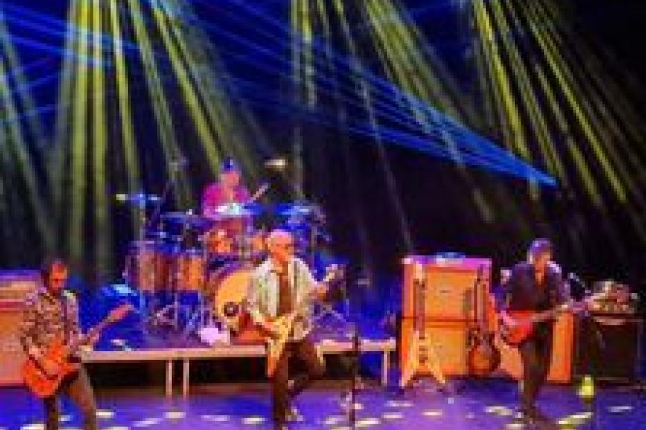 Eine Band spielt auf einer Bühne mit gelber und blauer Beleuchtung.