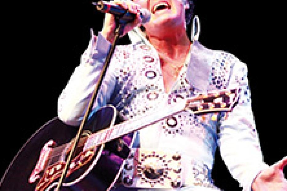 Ein Elvis-Presley-Imitator singt mit Gitarre auf einer Bühne.
