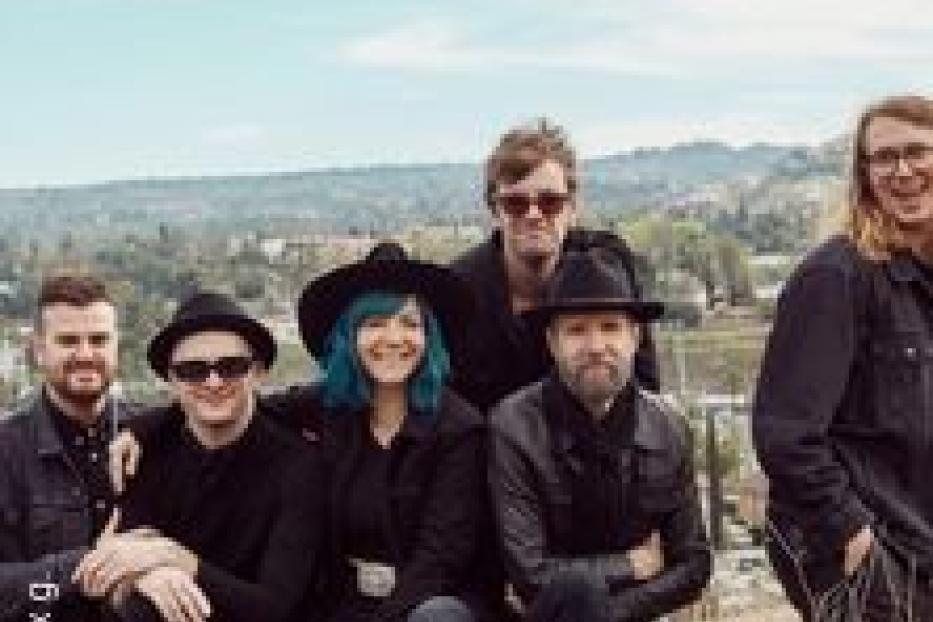 Eine Band sitzt vor einer Landschaft mit Hügeln und Bäumen.