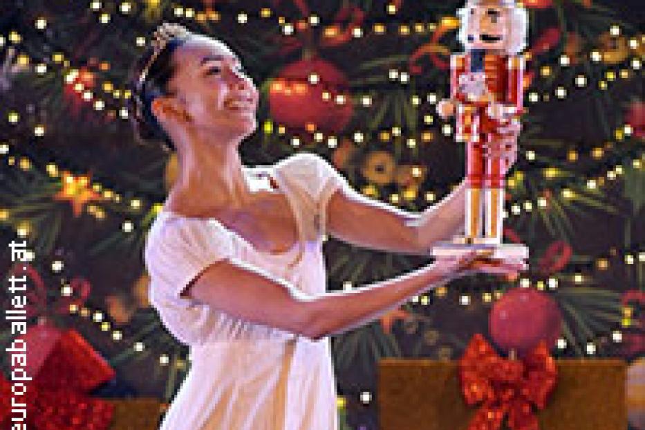 Eine Ballerina hält einen Nussknacker vor einem Weihnachtsbaum.
