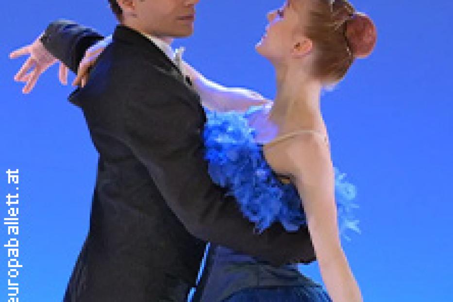 Ein Tänzerpaar in Kostümen tanzt vor einem blauen Hintergrund.