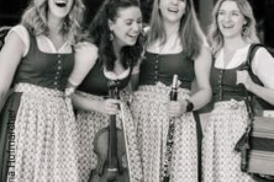 Vier Frauen in Dirndln lachen und halten Musikinstrumente.