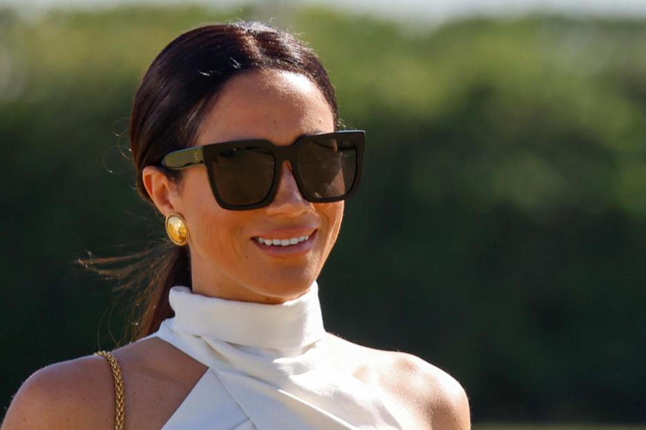 Herzogin Meghan mit dunkler Sonnenbrille und weißem Oberteil lächelt.