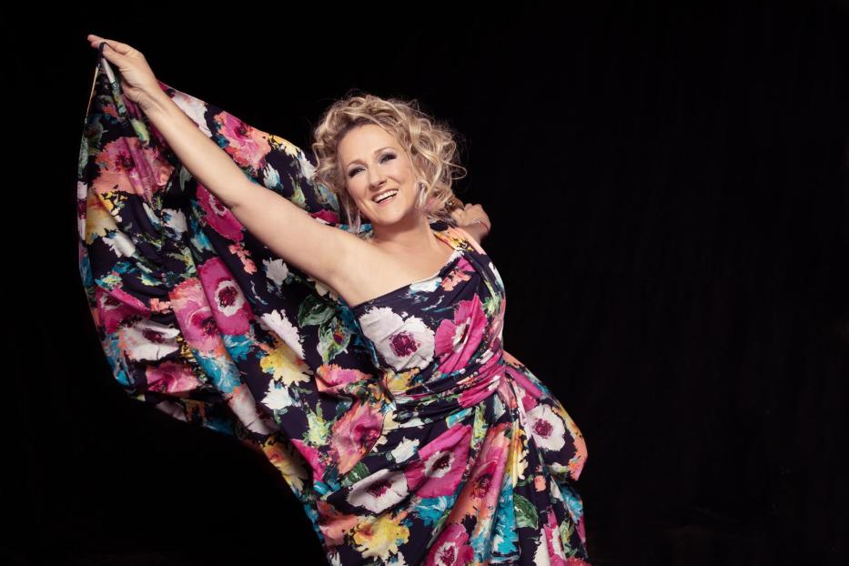 Eine Frau weht mit ihrem Kleid mit Blumenaufdruck und lächelt in die Kamera.