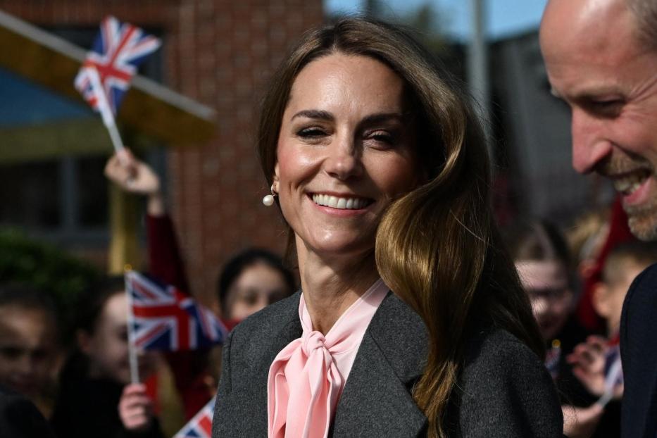 Kate, mit Blumenstrauß, lächelt neben William, während Kinder mit Union-Jack-Flaggen winken.