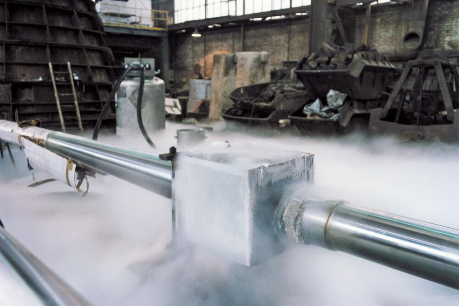 Metallrohre mit frostbedecktem Verbindungsstück, aus dem kalter Dampf entweicht, in einer Industriehalle.