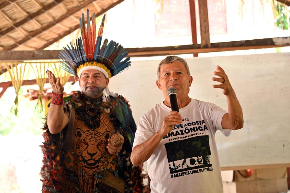 Zwei Männer, einer traditionell gekleidet, sprechen bei einer Versammlung im Amazonasgebiet.