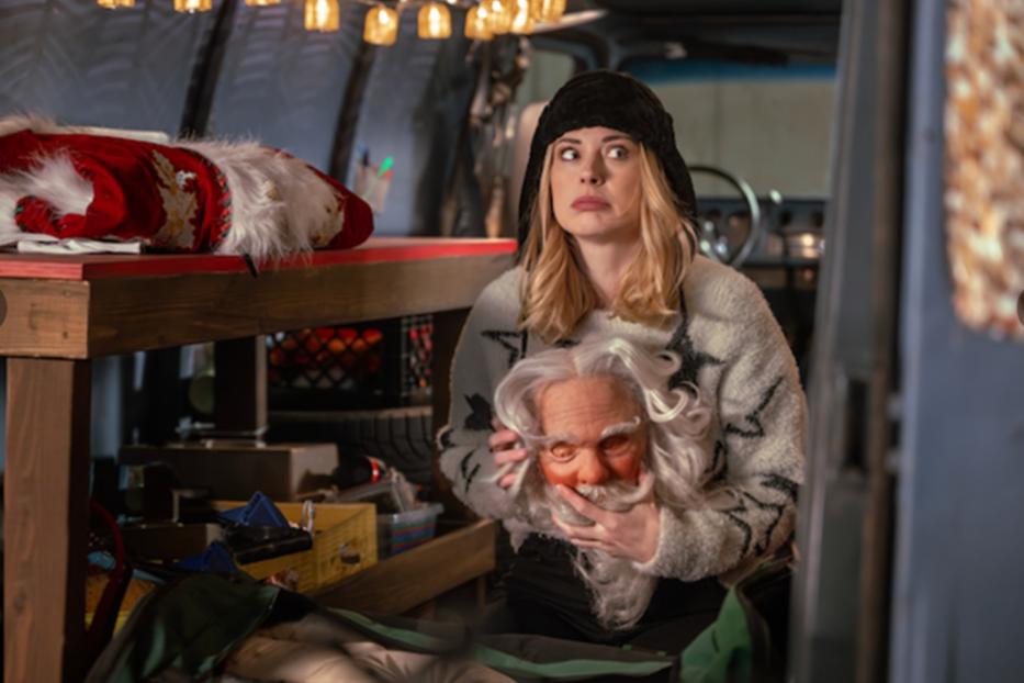 Frau in geöffnetem Laderaum eines Transporters, die eine Santa-Maske in den Händen hält