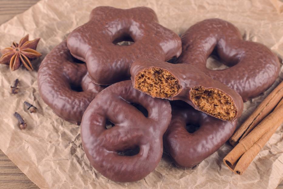 Mehrere mit Schokolade überzogene Lebkuchen in verschiedenen Formen liegen auf braunem Papier, daneben Zimtstangen und Sternanis.
