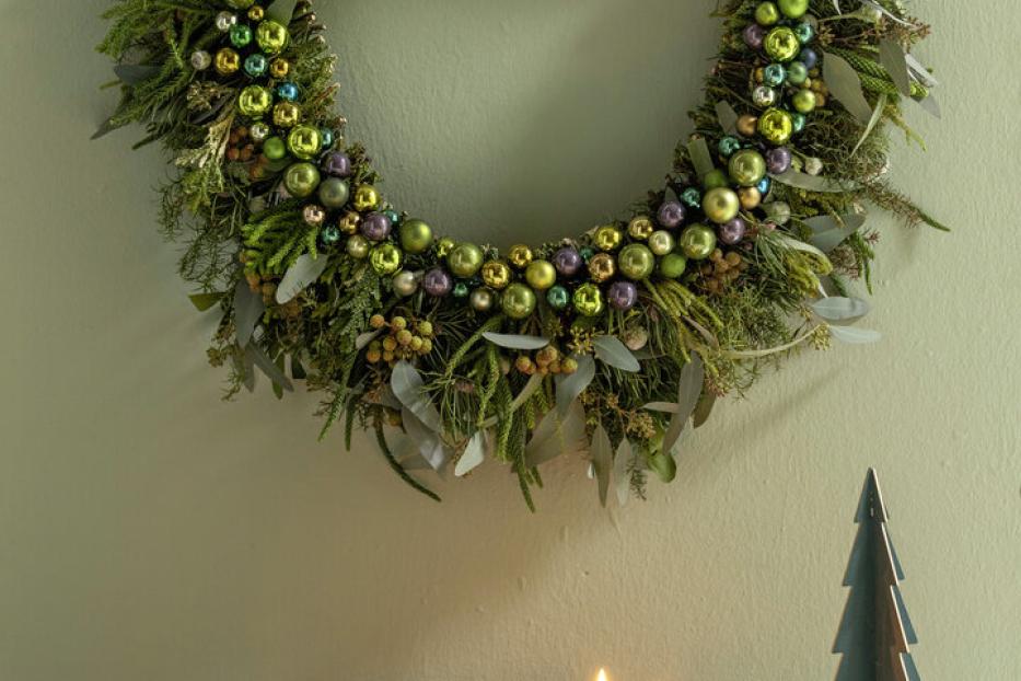 Dekorative Girlande: Tannenzweige werden mit glänzenden Kugeln in Grüntönen kombiniert, das ganze auf einem stabilen Ast befestigt. 
