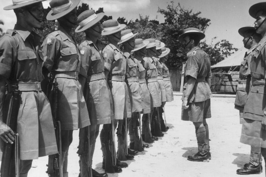 Soldaten in Uniform stehen in Reih und Glied und werden von einem Vorgesetzten auf dem Exerzierplatz inspiziert.