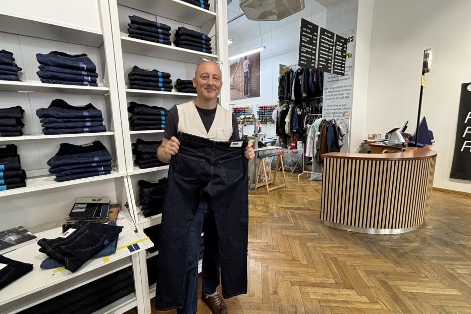 Mann in Jeansladen hält eine sehr große dunkle Jeans vor sich.