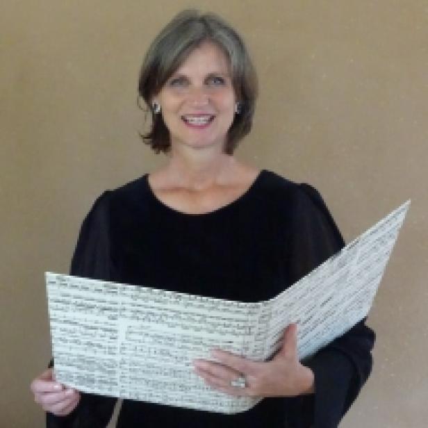 Eine Frau mittleren Alters hält ein aufgeschlagenes Notenbuch in ihren Händen.