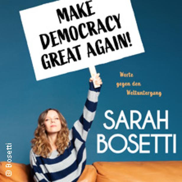 Sarah Bosetti hält ein Schild mit der Aufschrift „Make Democracy Great Again!“ hoch.